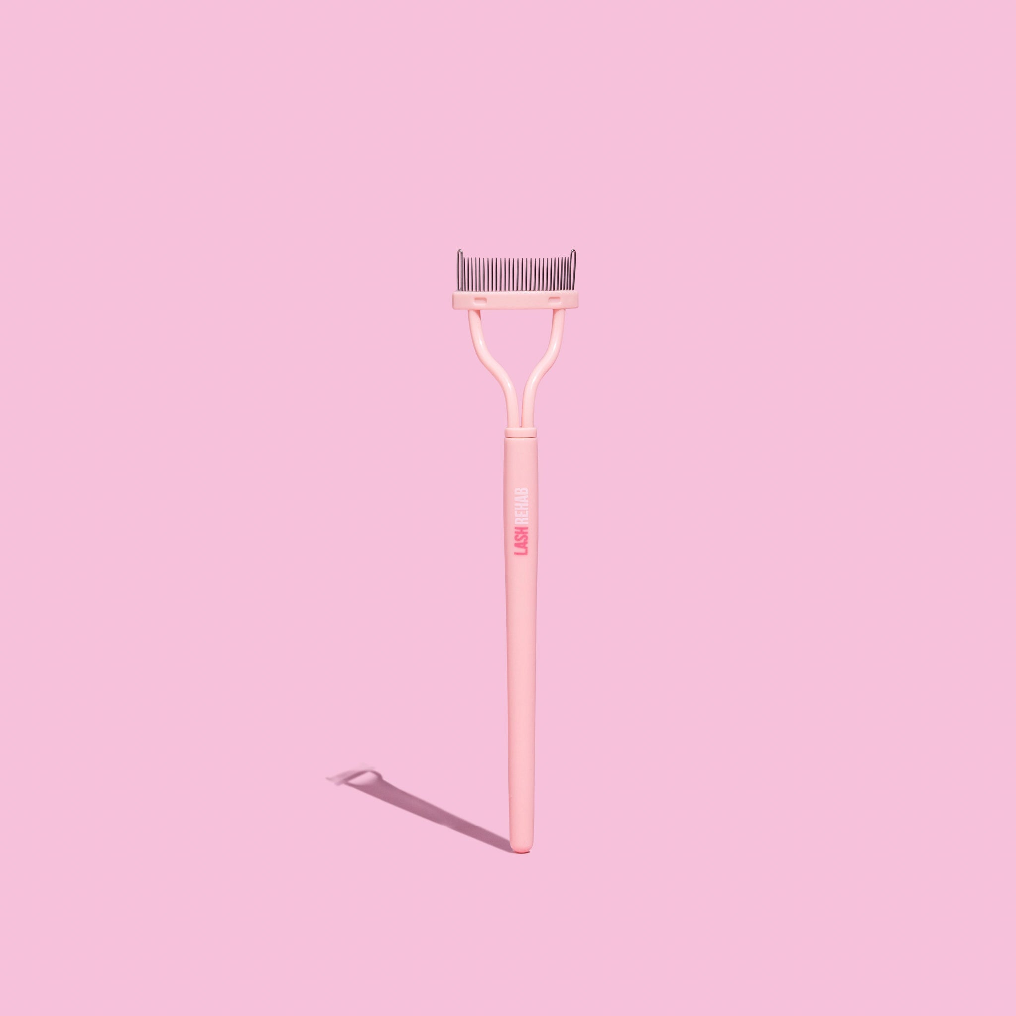 The Lash Rehab Lash Separator – precision lash comb tool for separating lashes and removing mascara clumps, shown on pink background.
