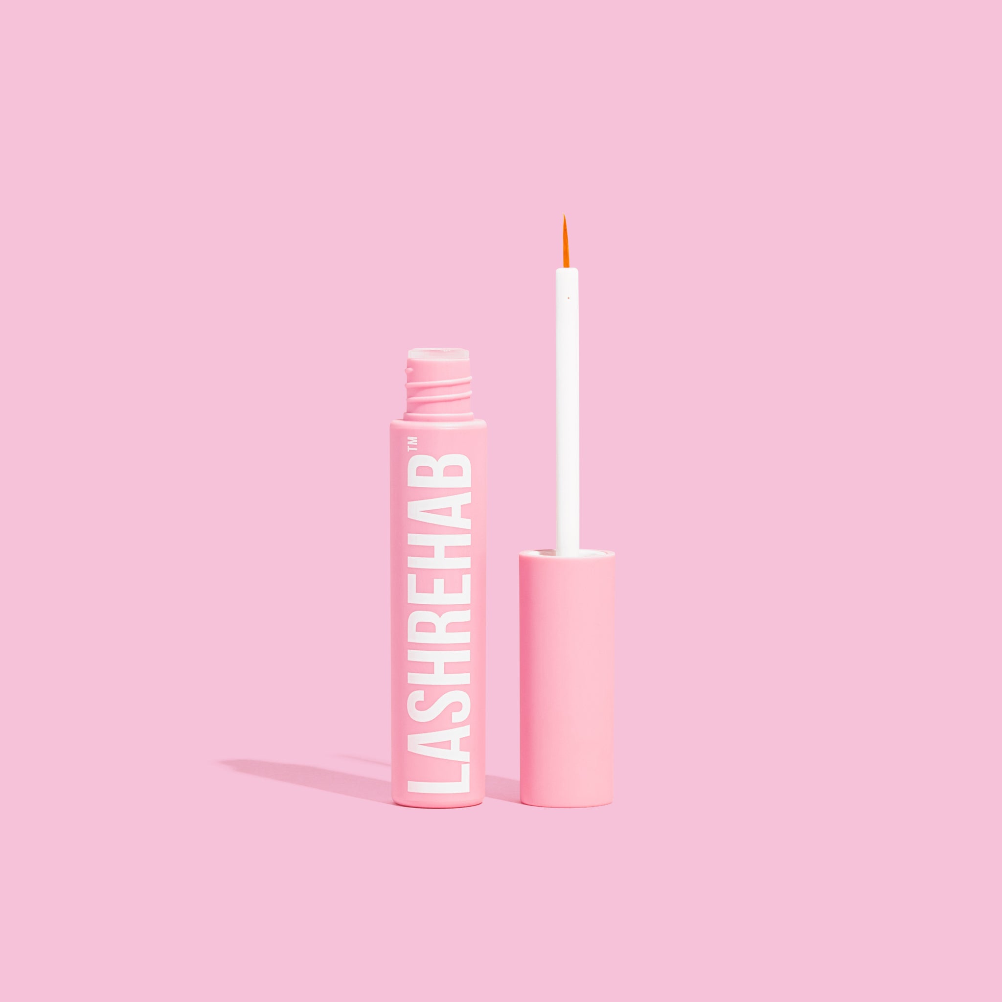 Lash Rehab Eyelash Growth Serum with applicator displayed upright on pastel pink background — vegan, clinically tested formula for natural lash enhancement.