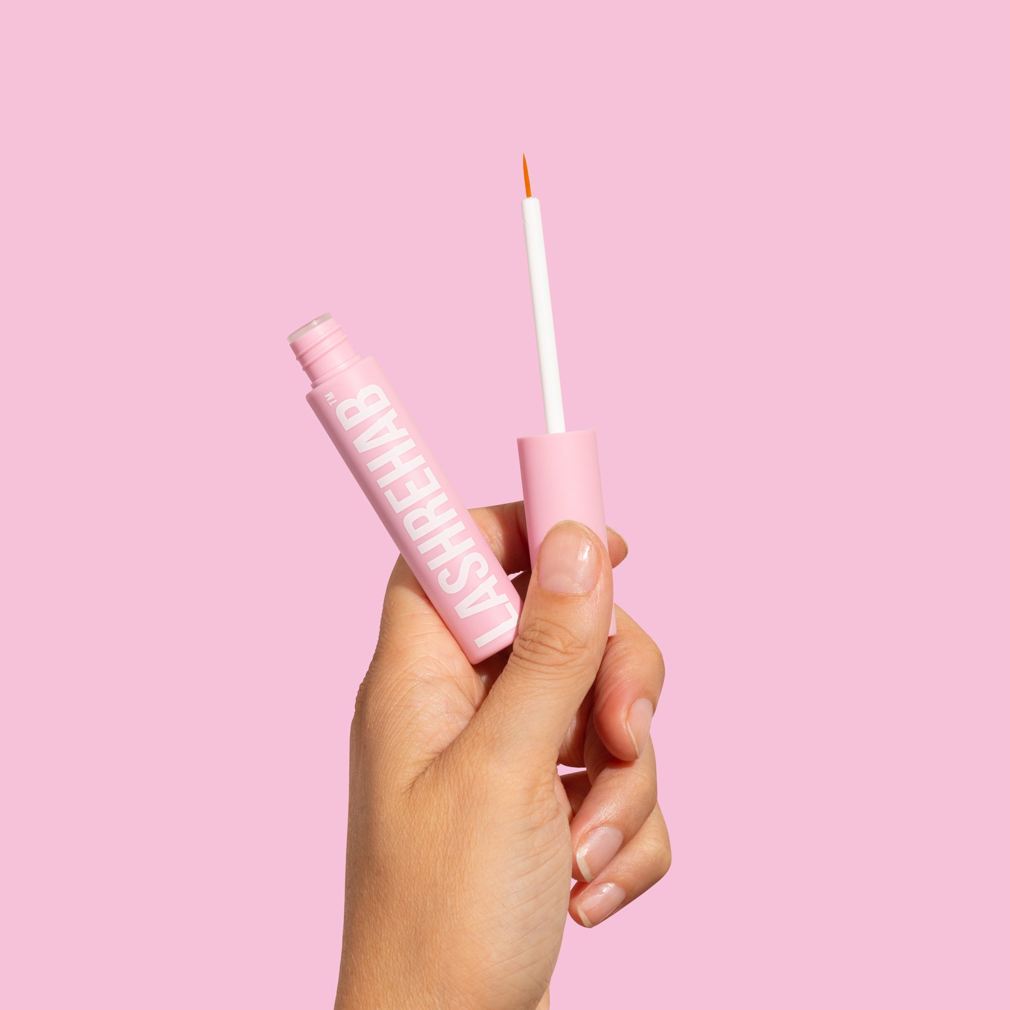 Hand holding Lash Rehab lash growth serum and applicator wand, demonstrating precise application and pink minimalist packaging.