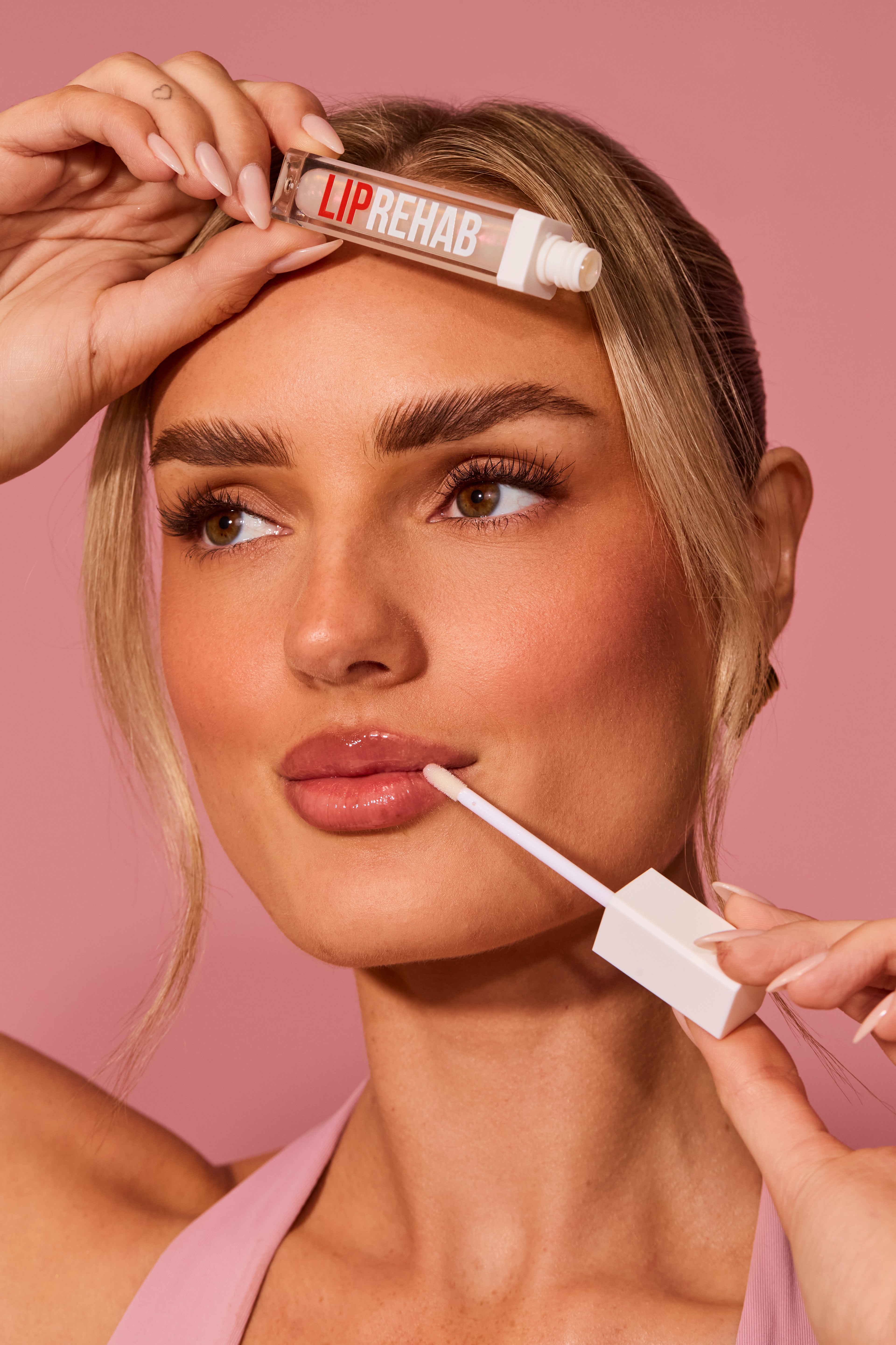 Model applying Lip Rehab lip plumper gloss for fuller, hydrated lips — featuring sleek applicator and bold branding